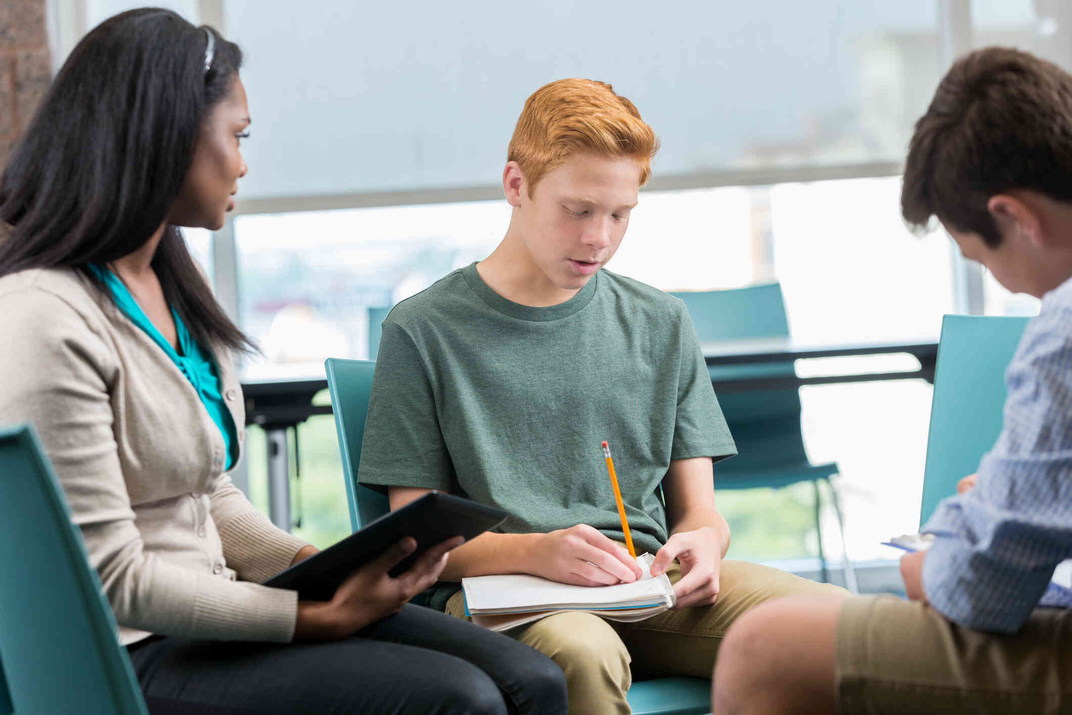 A young man talking while looking down at his notebook, appearing to be in a group session.